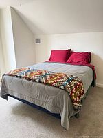 Queen bed assembled with grey duvet, patterned throw, red pillows and sheet on navy foundation