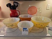 Group view of four Pyrex bowls, red Le Creuset pitcher with utensils, mason jar and lid