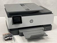 Front angled view of HP OfficeJet Pro 8025e printer with paper tray extended and four sealed ink cartridges