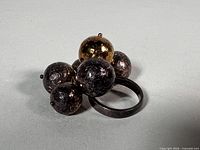 Ring with cluster showing five dark silver balls and one gold ball