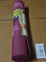 Rolled purple yoga mat in original wrap showing texture and maxsold lot tag