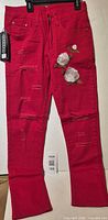 Full front view of red distressed embroidered jeans with hangtag visible