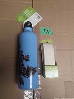 Blue aluminum water bottle and boxed cotton yoga strap side by side