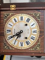 Front view of clock face showing Roman numerals, ornate corners, twin keyholes