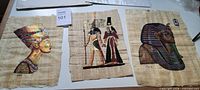 Three papyrus artworks laid out: Nefertiti, deity scene, Tutankhamun mask