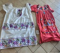 White and red embroidered dresses laid flat, full view
