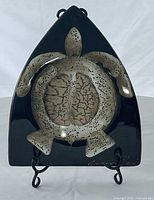 Front view of triangular plate on stand, showing turtle motif and signature
