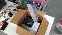 Open box showing all speakers including four silver cubes stacked, black rectangular unit, white cylindrical speaker