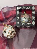 Both ornaments shown side by side; gold ornament in box, white ornament outside