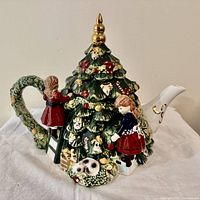 Front view of Christmas tree-shaped teapot with children figurines and decorations visible