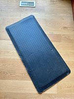 Full view of rectangular black anti-fatigue mat on wood floor