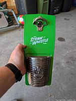 Front view of green Steam Whistle metal sign showing opener and cap catcher
