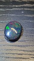 Front view of oval black opal showing multicolor play-of-color