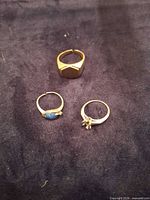 Three 14K yellow gold rings arranged on dark cloth