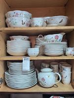 Dinnerware stacks on shelving showing plates, bowls, mugs, serving bowls, teapot and accessories