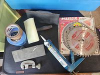 Assorted tools and consumables laid out including tape rolls, sanding items, caulking gun, tubing cutter, saw blades