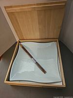 Open wooden box showing two ceramic plates and chopsticks