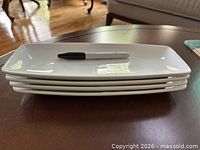 Stacked side view of four white porcelain platters with marker for scale