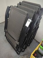Stack of four folded black and gray mesh patio chairs