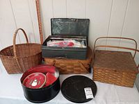 group shot of three picnic baskets, metal toolbox, film reel can, cookie tin and utensils