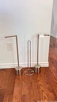 Three brushed nickel freestanding bathroom accessories on hardwood floor