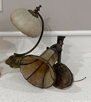 Brass alabaster shade sconce beside slag glass sconce on countertop