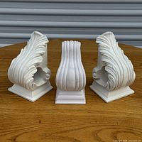 Front view of three white carved wooden corbels on table