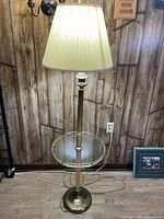 Full view of brass floor lamp with glass table shelf and shade