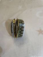 Side view of heart-shaped porcelain box slightly open, showing green floral band and brass hinge