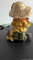 Rear view of scarecrow figurine showing straw hat, yellow blouse and gourd cluster