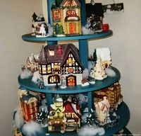 Full view of three tiers with multiple ceramic village buildings on teal wooden stand