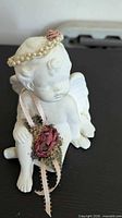 Front-left view of seated white ceramic cherub with faux pearl halo and floral ribbon detail