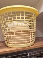 Yellow plastic mesh laundry hamper on shelf