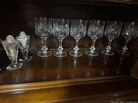 Six stemmed goblets and two shakers arranged in cabinet