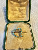 Front view of heart brooch in case showing turquoise and pearl settings