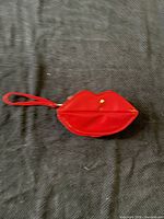 Front view of red lip-shaped handbag showing wrist strap and glossy finish