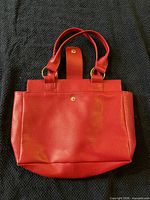 Front view of red purse showing snap-tab and handles