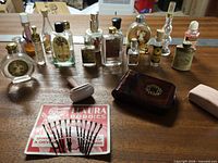 Group shot of all miniature perfume bottles, Coty compact (closed), Luxura bobby pins, safety razor, electric shaver and case