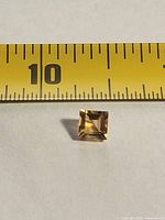 Front view of square faceted citrine beside tape measure