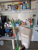 Overview of three shelves with chemicals, mop, broom, trash bin