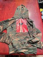 Full view of camo hoodie laid flat showing overall condition, drawstring hood, kangaroo pocket