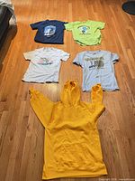 Group shot of all five garments laid flat: four T-shirts above, yellow hoodie below