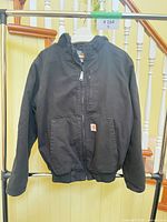 Front view of black Carhartt hooded jacket on rack
