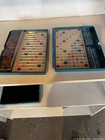 Two blue plastic Scrabble cases open showing boards, racks and tiles