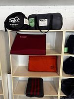 All items on shelving: Trekk sleeping bag in black sack, Chinook blanket in gray roll, red Therm-a-Rest pad