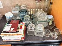 Group view of glass jars, bakeware, spice vials rack, oil bottle and cookbook stack on countertop