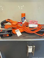 Leaf blower with battery attached, charger, extension cord and adhesive items on cabinet