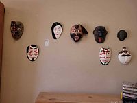 Eight masks mounted on wall above shelf