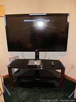 Overview of the LG 55 inch TV set on a black glass TV stand with remote and a small device on top.