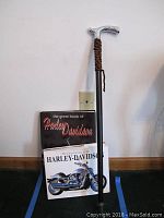 Walking stick with silver engraved handle and two Harley Davidson collectible books stacked against a wall